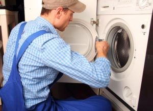Washing machine repair technician in blue overalls servicing an appliance for Carter Services in Torrance, California.