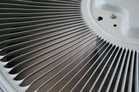Close-up of air conditioning unit fan blades, emphasizing maintenance importance for preventing emergency AC repairs during summer.