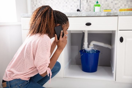 Young woman focused on plumbing issue with water leakage at kitchen sink, highlighting Carter Services plumbing solutions.