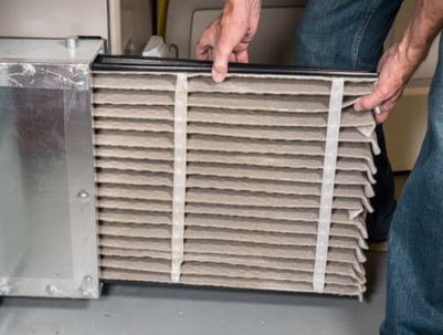 Person inserting a folded air filter into an HVAC unit, demonstrating proper maintenance for optimal indoor air quality.