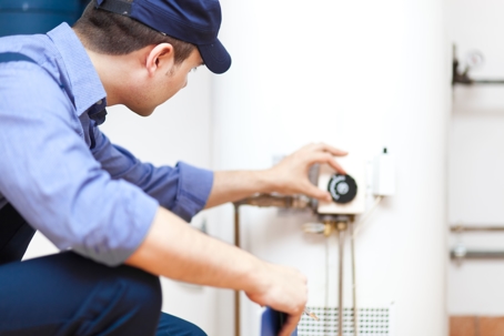 Technician in uniform examining water heater controls for Carter Services in Torrance, CA. Tools are visible nearby.