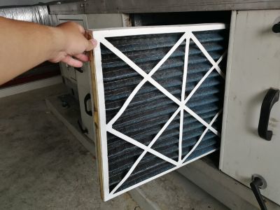 Hand holding a dirty air filter being removed from an HVAC unit, highlighting the importance of regular air filter replacement for improved indoor air quality and efficient heating and cooling systems.
