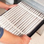 Person replacing an air filter in an HVAC system to improve indoor air quality and reduce allergy symptoms.