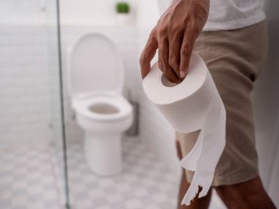 Person holding a roll of toilet paper in a bathroom, emphasizing proper use to prevent toilet clogs.
