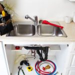 Kitchen sink with plumbing tools and supplies, including a red wrench, under-sink plumbing setup, and maintenance items, illustrating plumbing maintenance for homeowners.