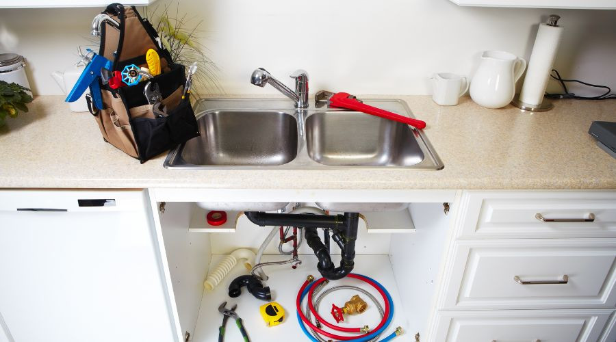 Plumbing tools and equipment near a kitchen sink, highlighting maintenance essentials for efficient plumbing service.